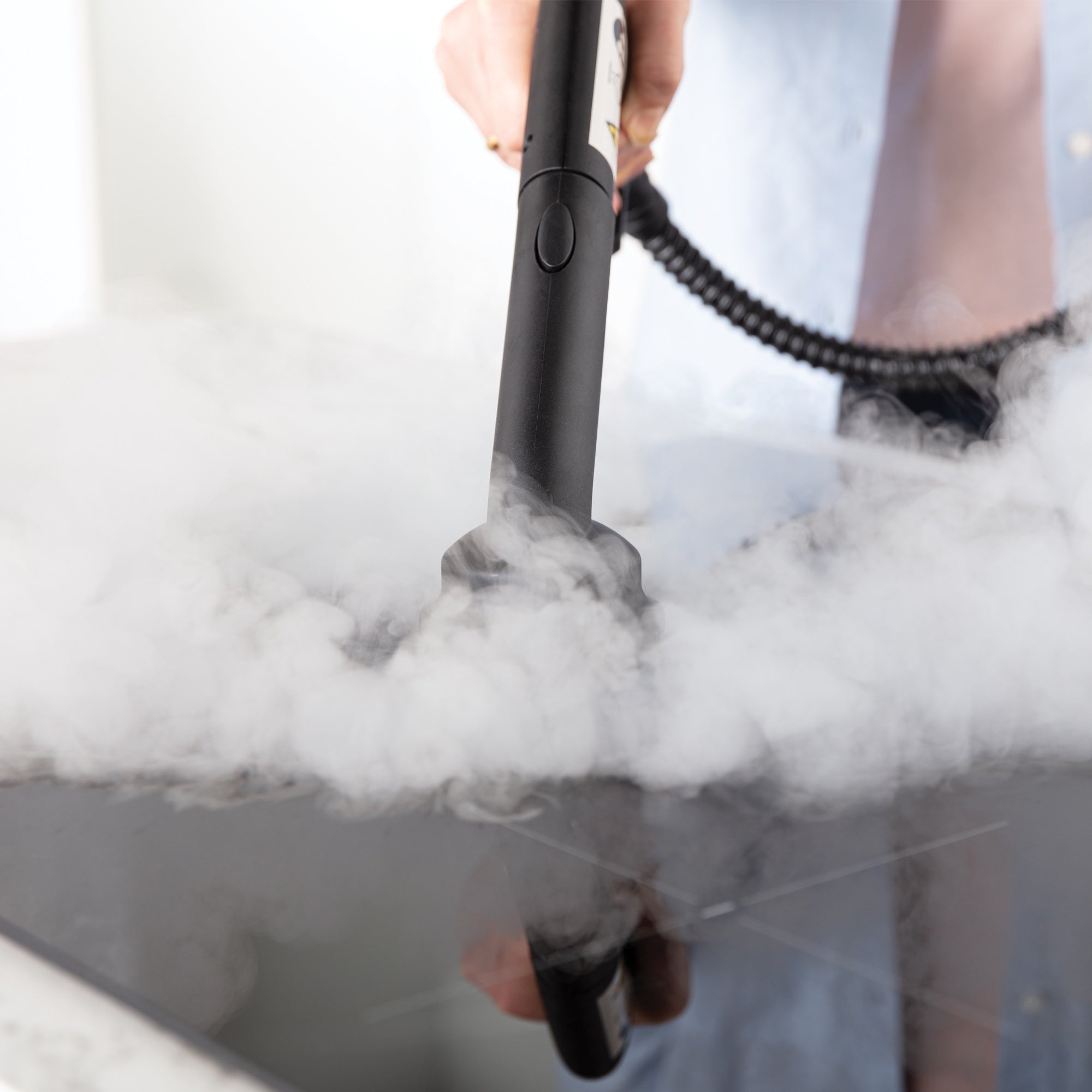 A person uses the STEAMDYNAMO+ 2000W Steam Cleaner & Sanitiser for chemical-free cleaning on a glass stovetop, holding the handle with a light blue sleeve while steam visibly covers the surface.