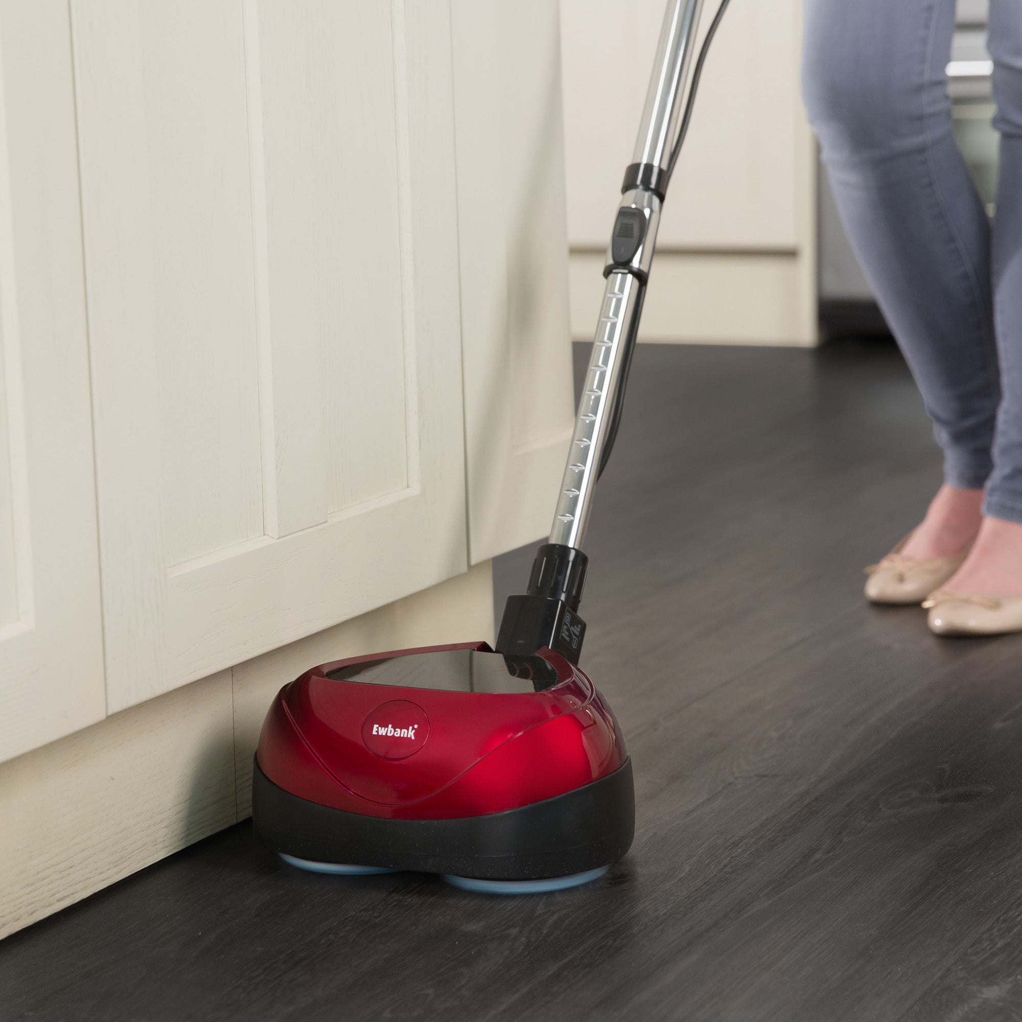 A person uses the EP170 Multi Use 3-in-1 Floor Cleaner & Polisher with a long handle to clean a dark wood floor near white cabinets, only their legs and feet visible.