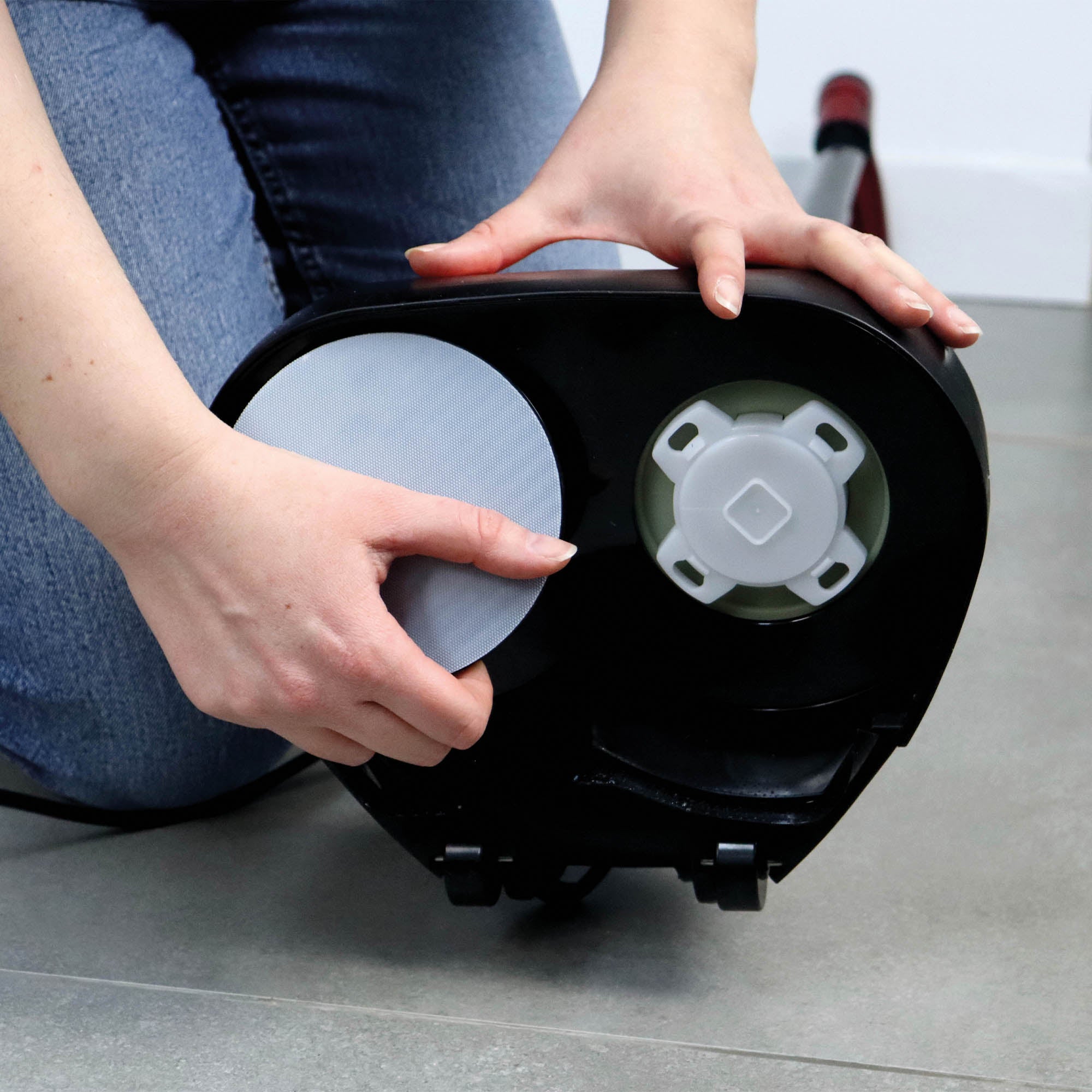 A person kneels on a tiled floor to attach a round cleaning pad to the base of the EP170 Multi Use 3-in-1 Floor Cleaner & Polisher.