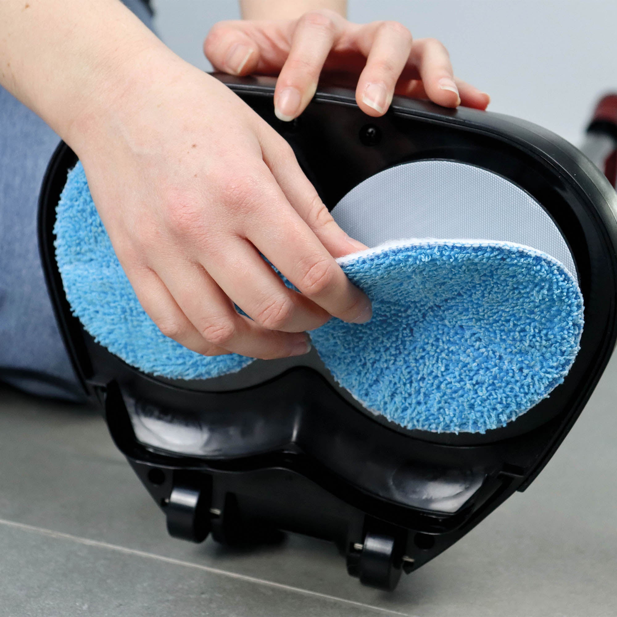 A person attaches a round blue microfiber pad to the underside of a black EP170 Multi Use 3-in-1 Floor Cleaner & Polisher on a gray tiled floor.