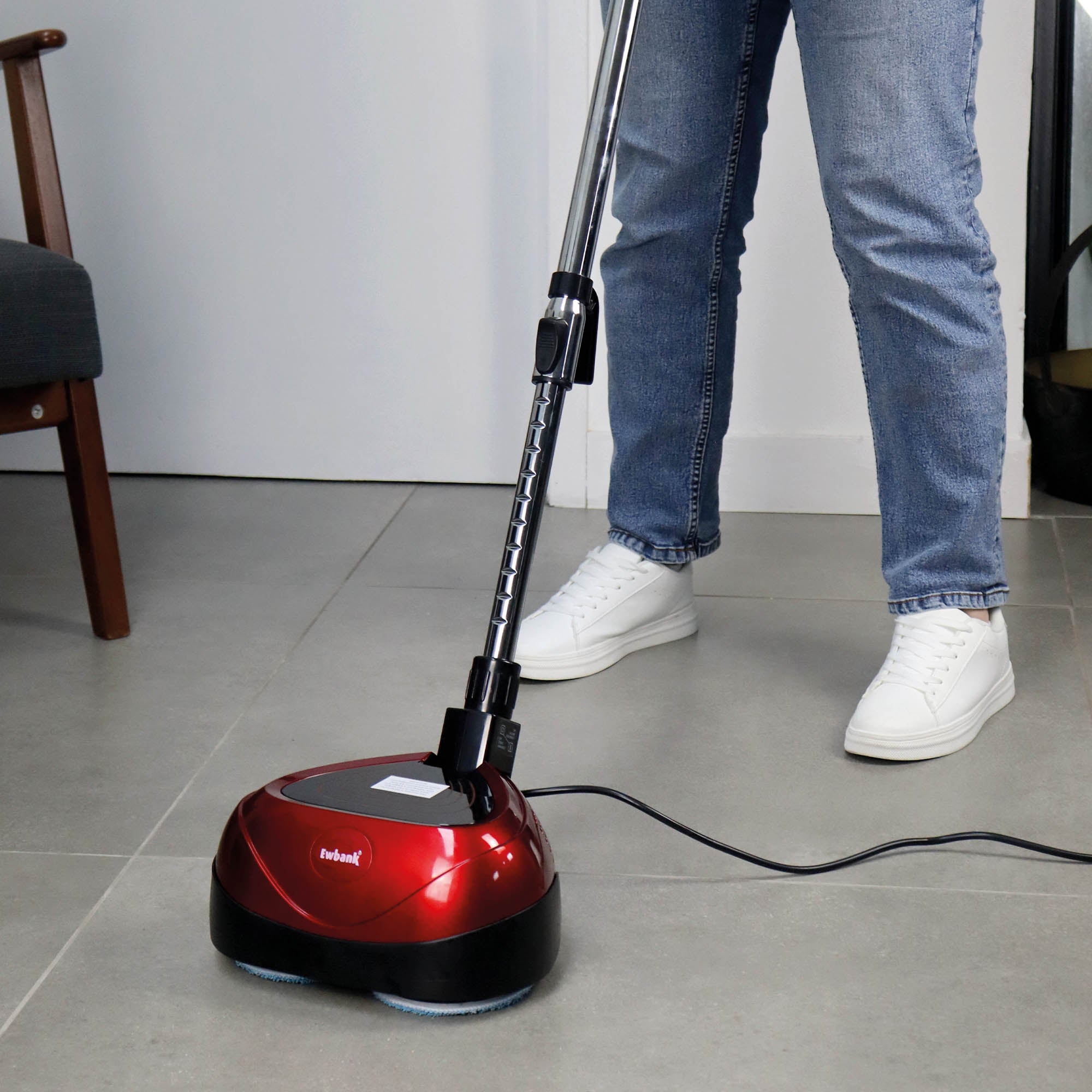 A person in white sneakers and blue jeans is using the EP170 Multi Use 3-in-1 Floor Cleaner & Polisher on a gray tiled floor. Only the lower half of the person is visible, and the device is plugged in.