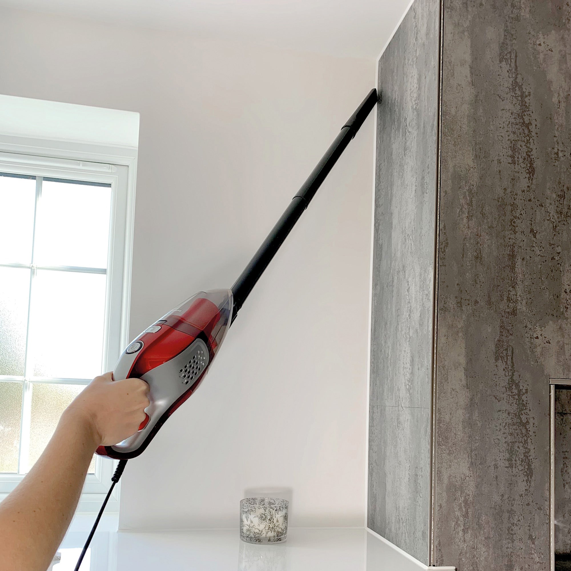 Person using a steam cleaner on a kitchen cabinet.