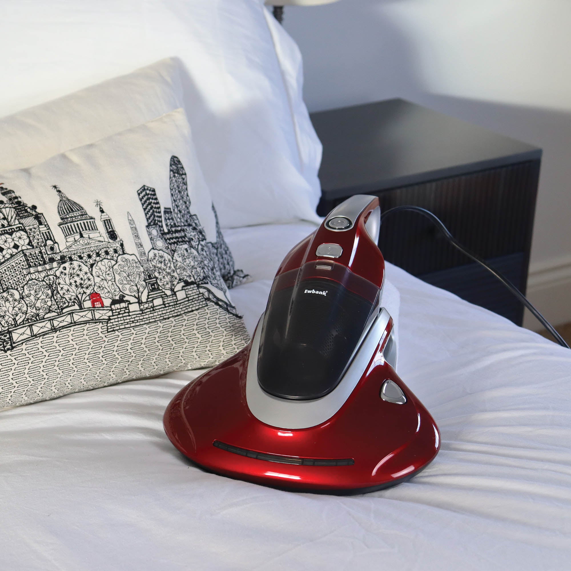 Red and white vacuum cleaner on a bed with a decorative pillow in the background