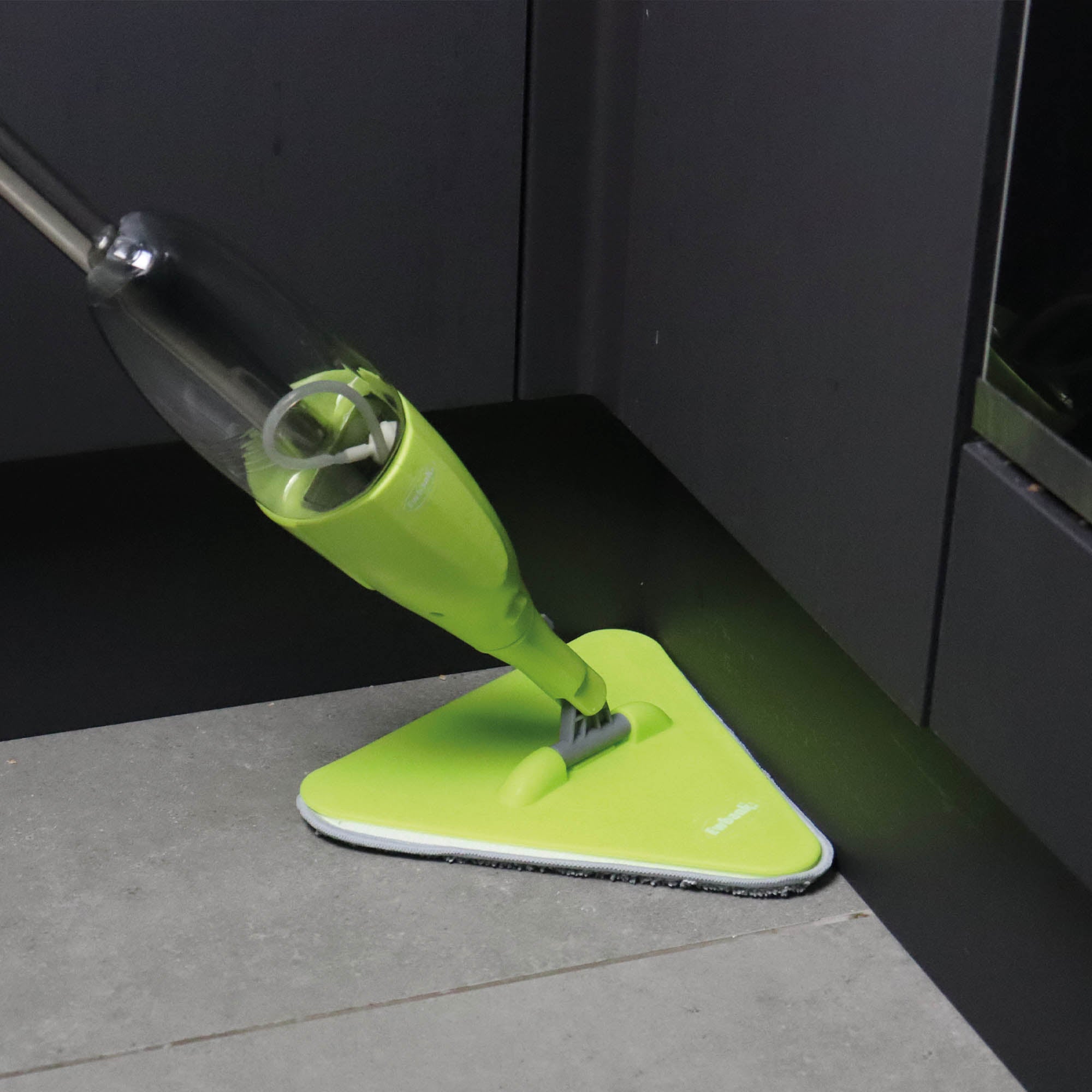 The 5-in-1 Universal Spray Mop Set by Ewbank in green, featuring interchangeable heads and a trigger spray, easily cleans tight corners where gray tiles meet dark cabinetry, making it ideal for hard-to-reach spaces.