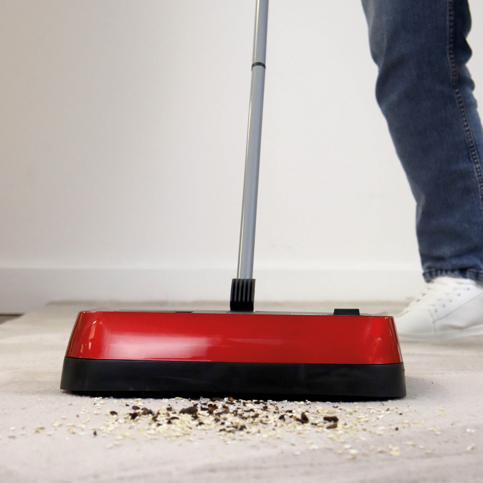Person using a red and black floor cleaning tool on a carpeted floor.