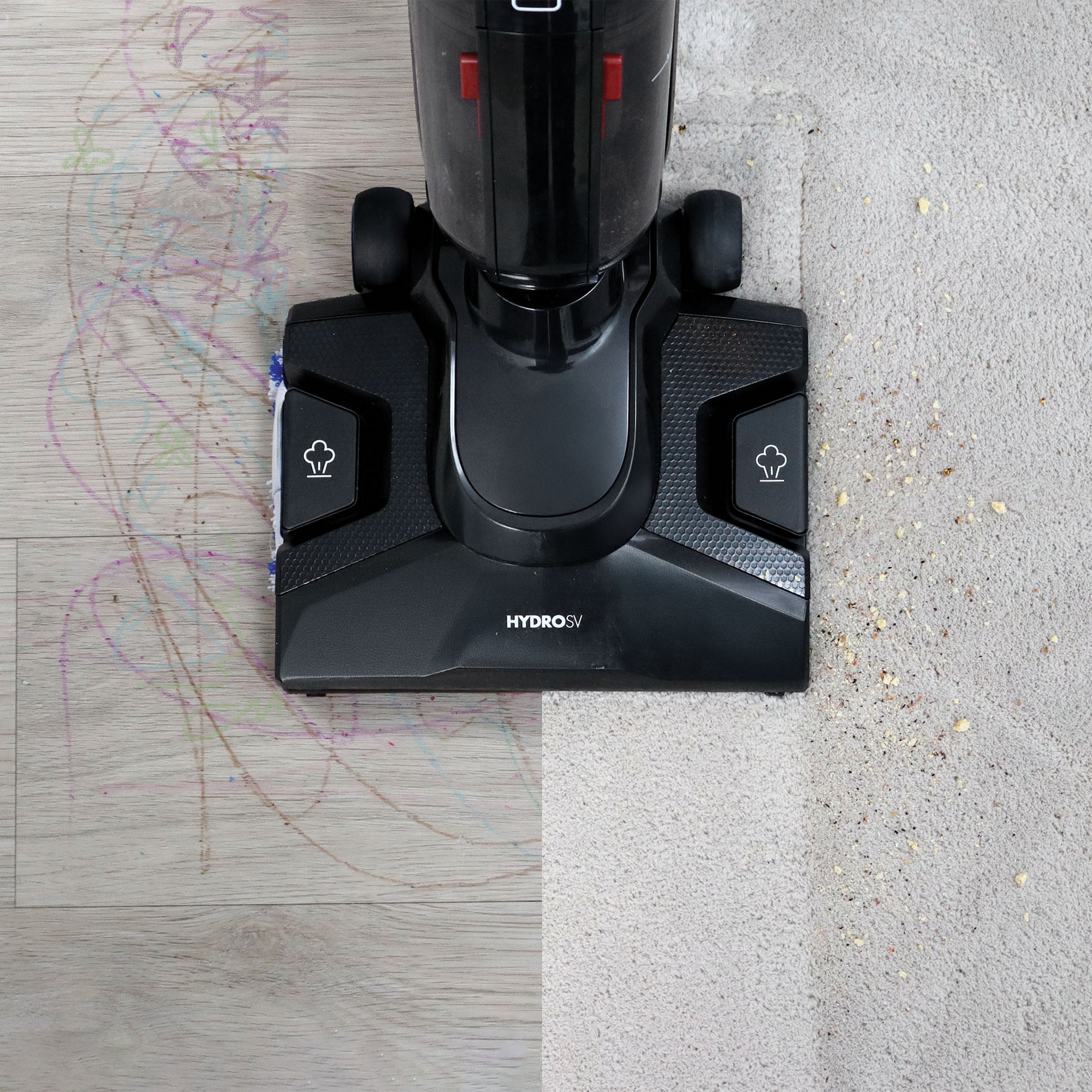 The Ewbank HYDROSV 2-In-1 Steam Vacuum Cleaner, Black is shown cleaning a wood floor with colorful scribbles on the left and a crumb-covered carpet on the right, both revealing a spotless path where the vacuum has passed.