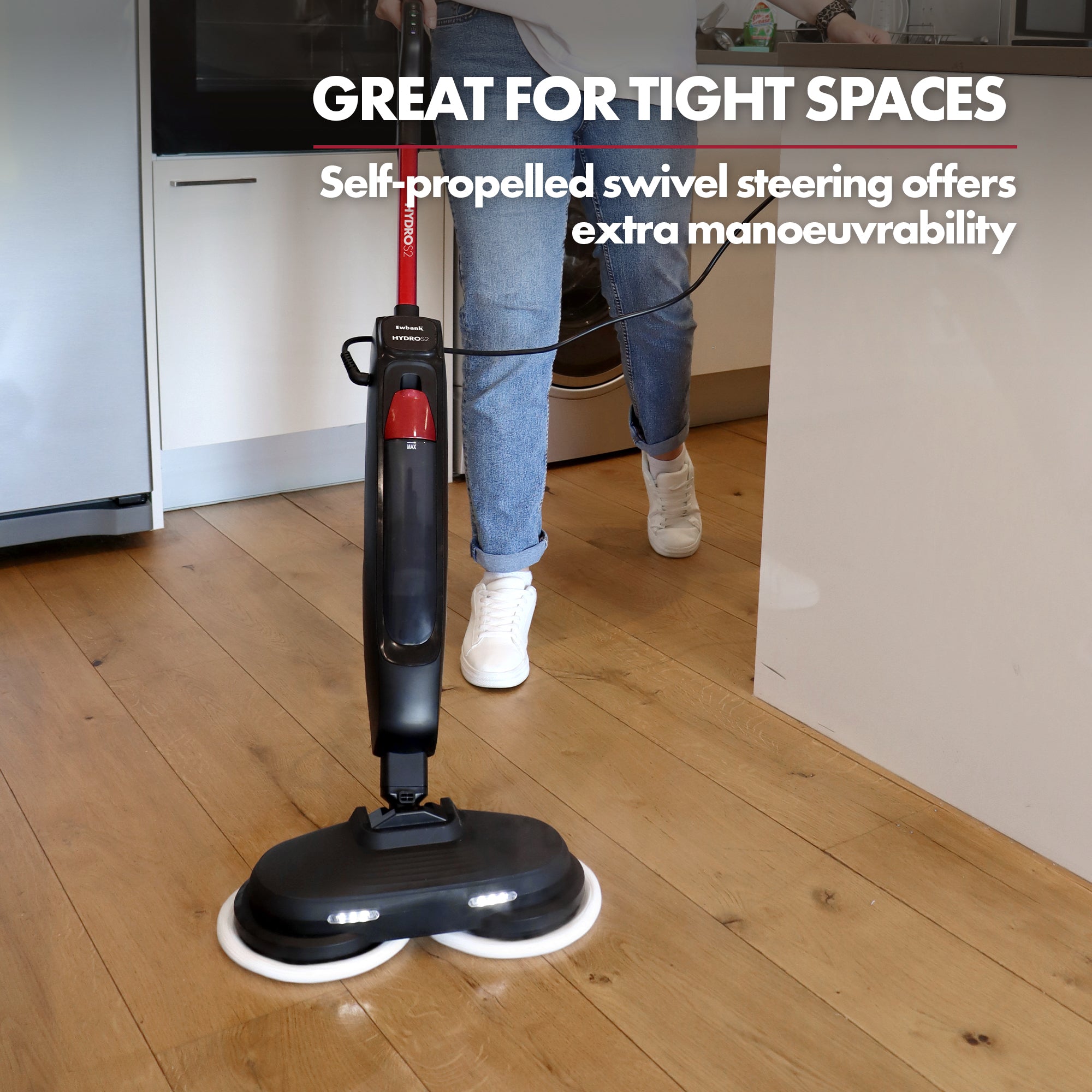 A person uses the Ewbank EWST04079 HYDROS2 Steam and Spin Mop with 1500W power and 220RPM rotating pads on a wooden kitchen floor. Text: Great for tight spaces. Self-propelled swivel steering makes hard floor cleaning easy.