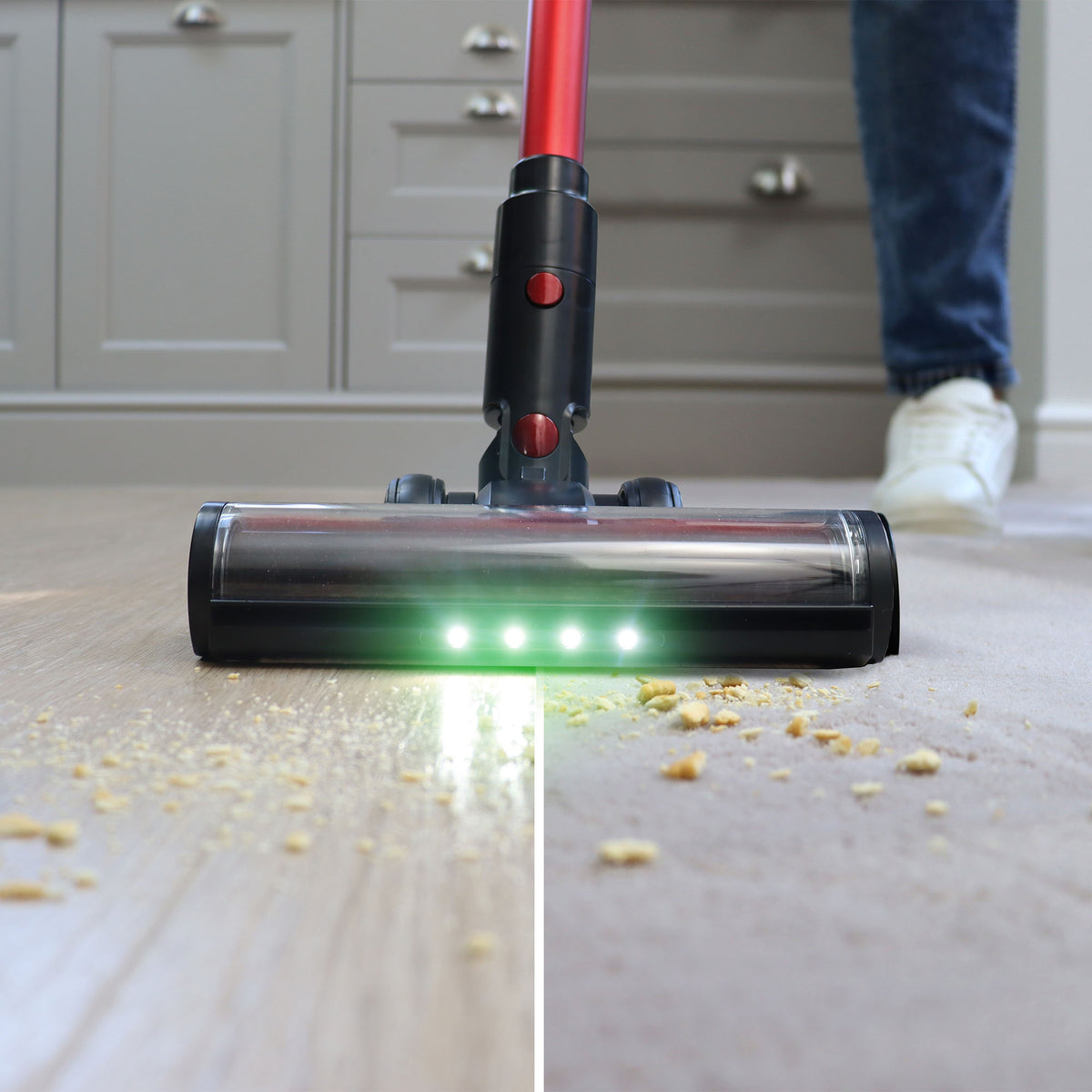 The AIRSTORM AUTO Empty Cordless Stick Vacuum Cleaner—with LED lights and an eco-friendly reusable dust bag—is shown cleaning crumbs from a wooden floor, revealing a clear difference between the cleaned and uncleaned areas as a person’s foot appears in the background.