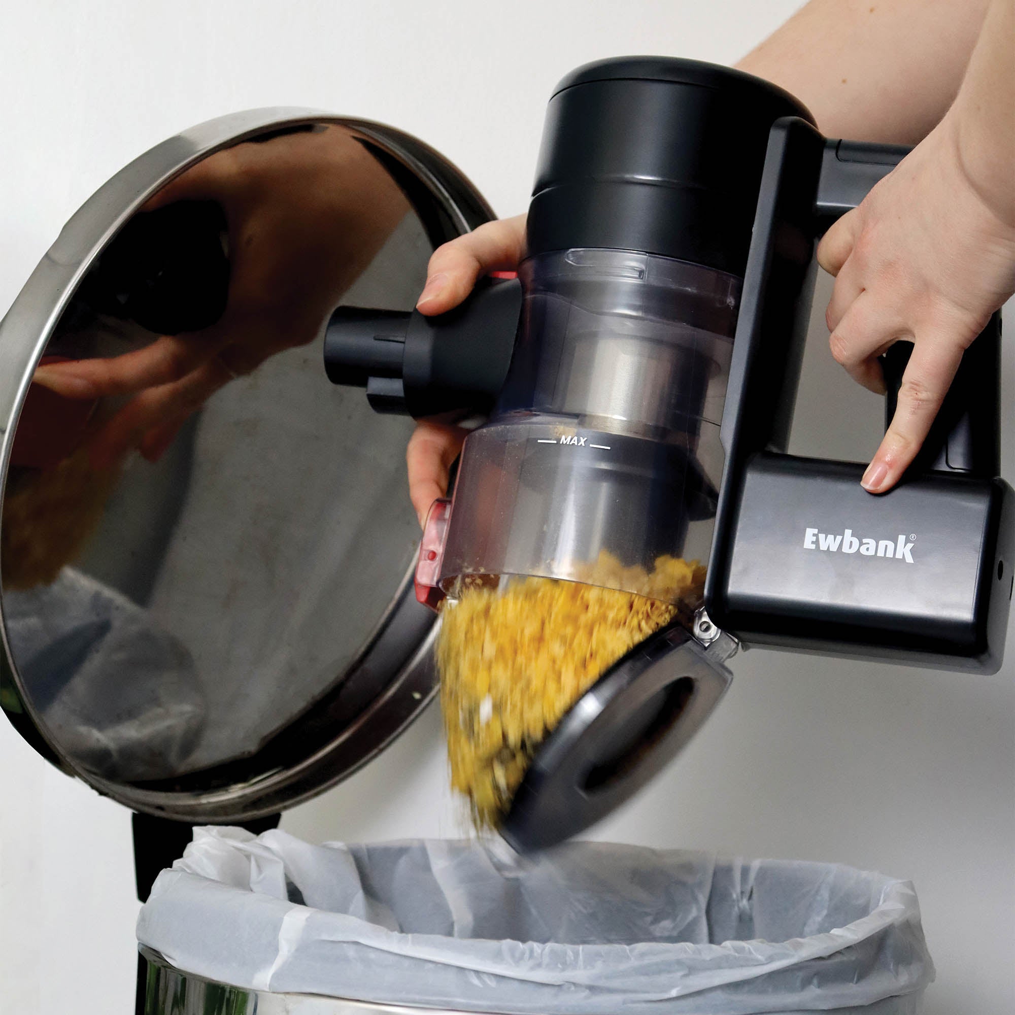A person empties an AIRBLITZ 2-in-1 Cordless Stick Vacuum Cleaner full of debris into a white trash bag, with their reflection visible on the can's lid.