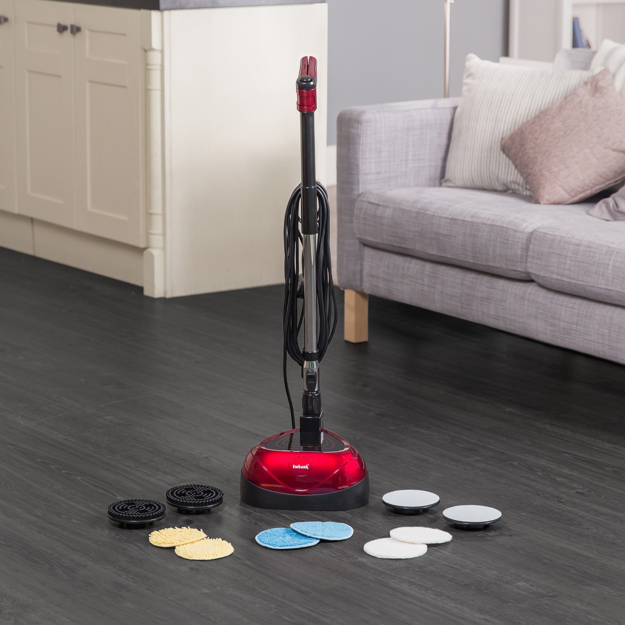 The EP170 Multi Use 3-in-1 Floor Cleaner & Polisher in red and black stands on dark wood flooring, with multiple cleaning pads and attachments nearby. A light gray sofa and kitchen cabinets appear in the background.