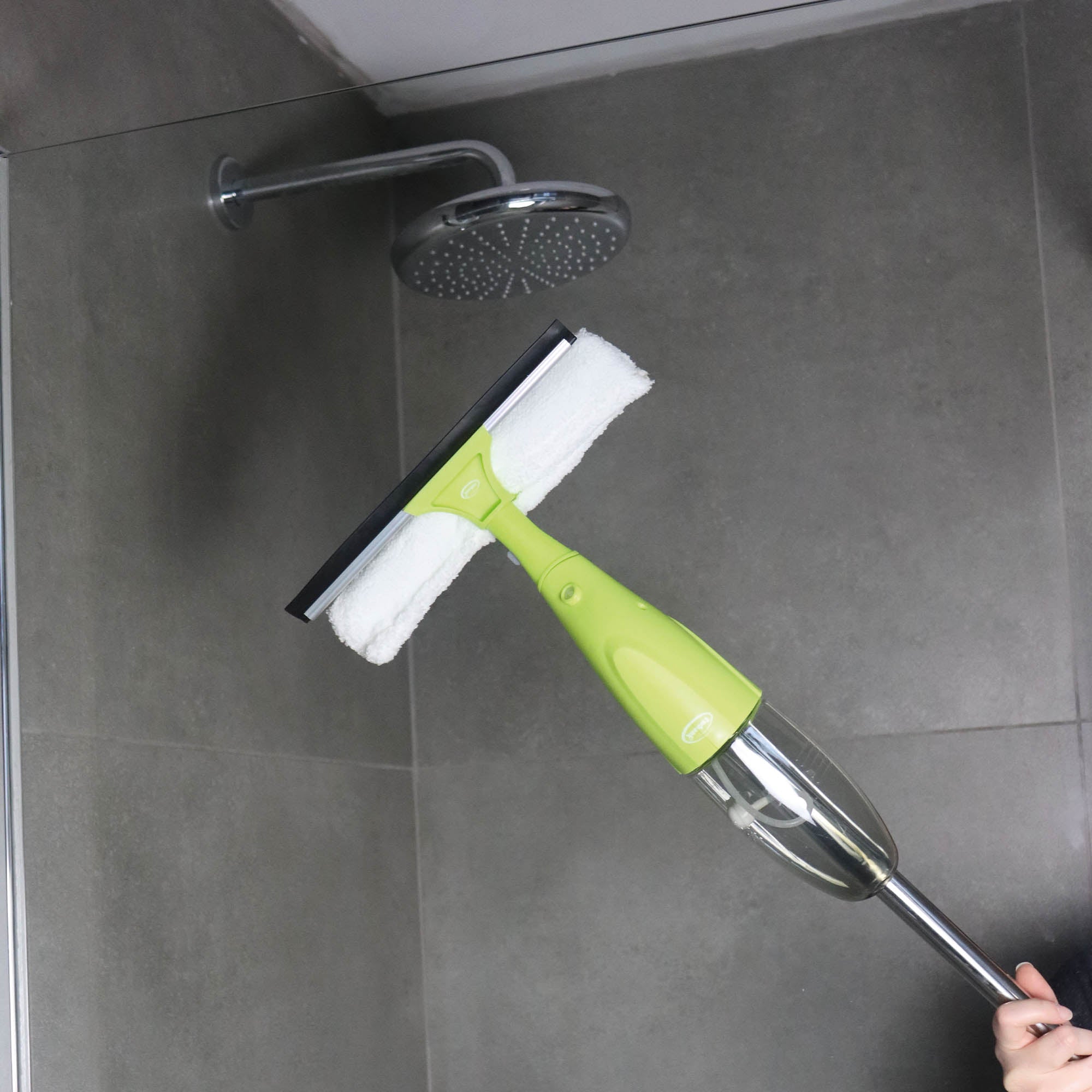 A person uses the Ewbank 5-in-1 Universal Spray Mop Set with green interchangeable heads and trigger spray to clean a gray tiled shower wall under a round showerhead.