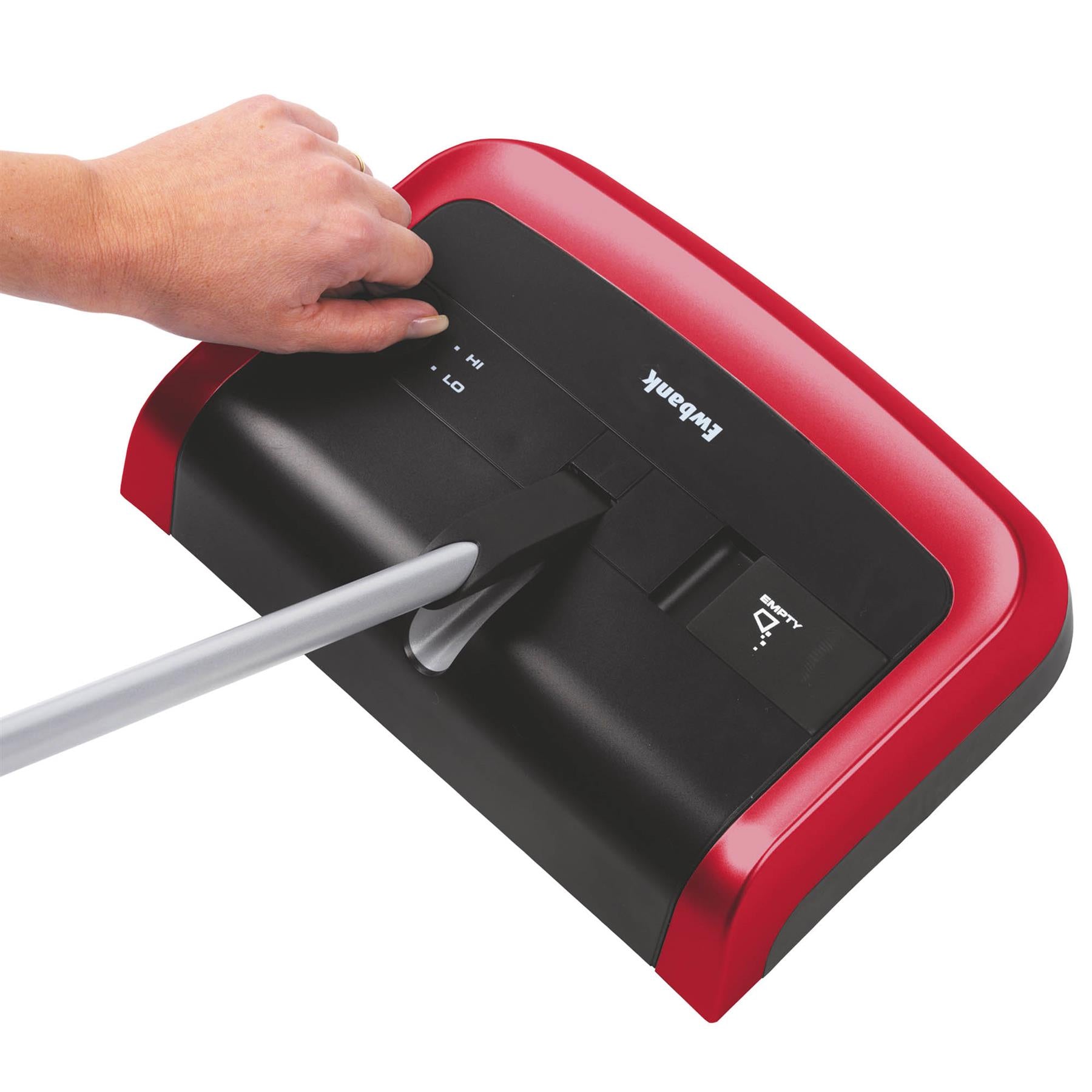 A hand adjusts the brush height on the Evo3 Manual Carpet Sweeper, a red and black device with a handle, designed for hygienic cleaning of both carpet and hard floors.