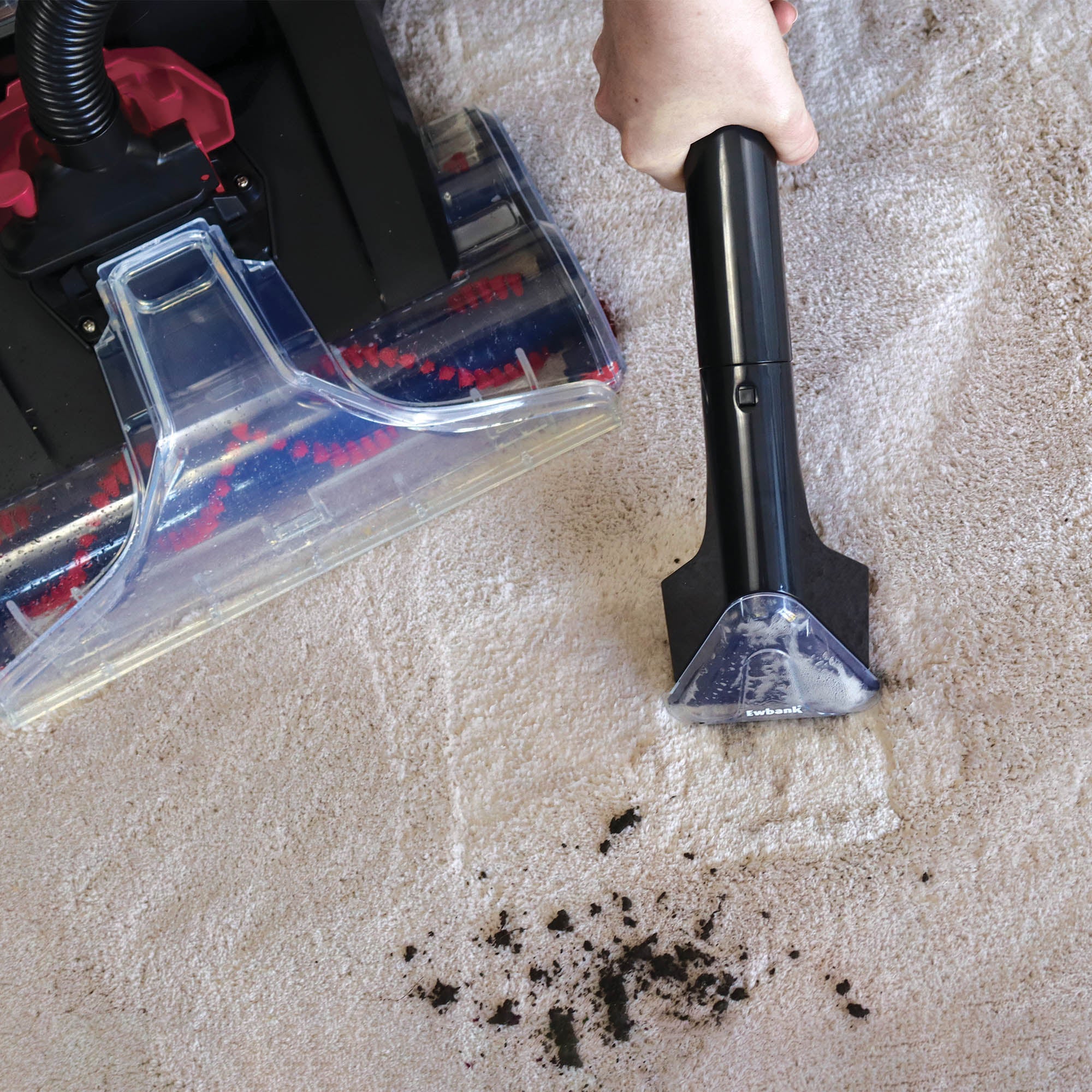 A hand uses the HYDROC2 Carpet & Upholstery Cleaner with a handheld attachment to remove dirt and debris from a light-colored carpet, while the main HYDROC2 machine is visible nearby.