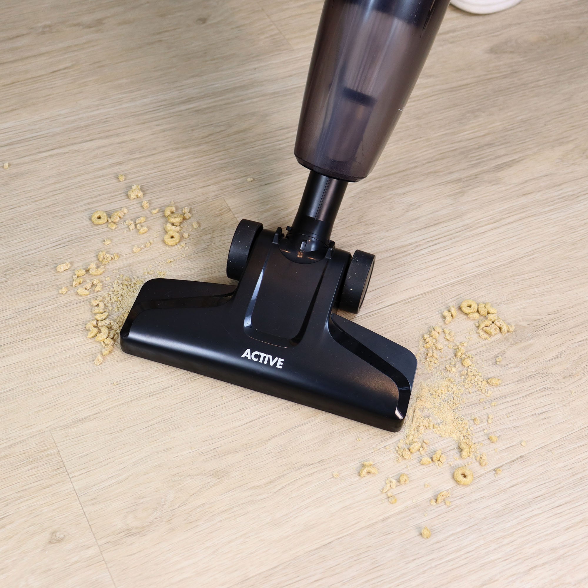 The ACTIVE 2-in-1 Corded Stick Vacuum Cleaner, Red/Black is being used to clean spilled cereal and crumbs from a light wood floor.