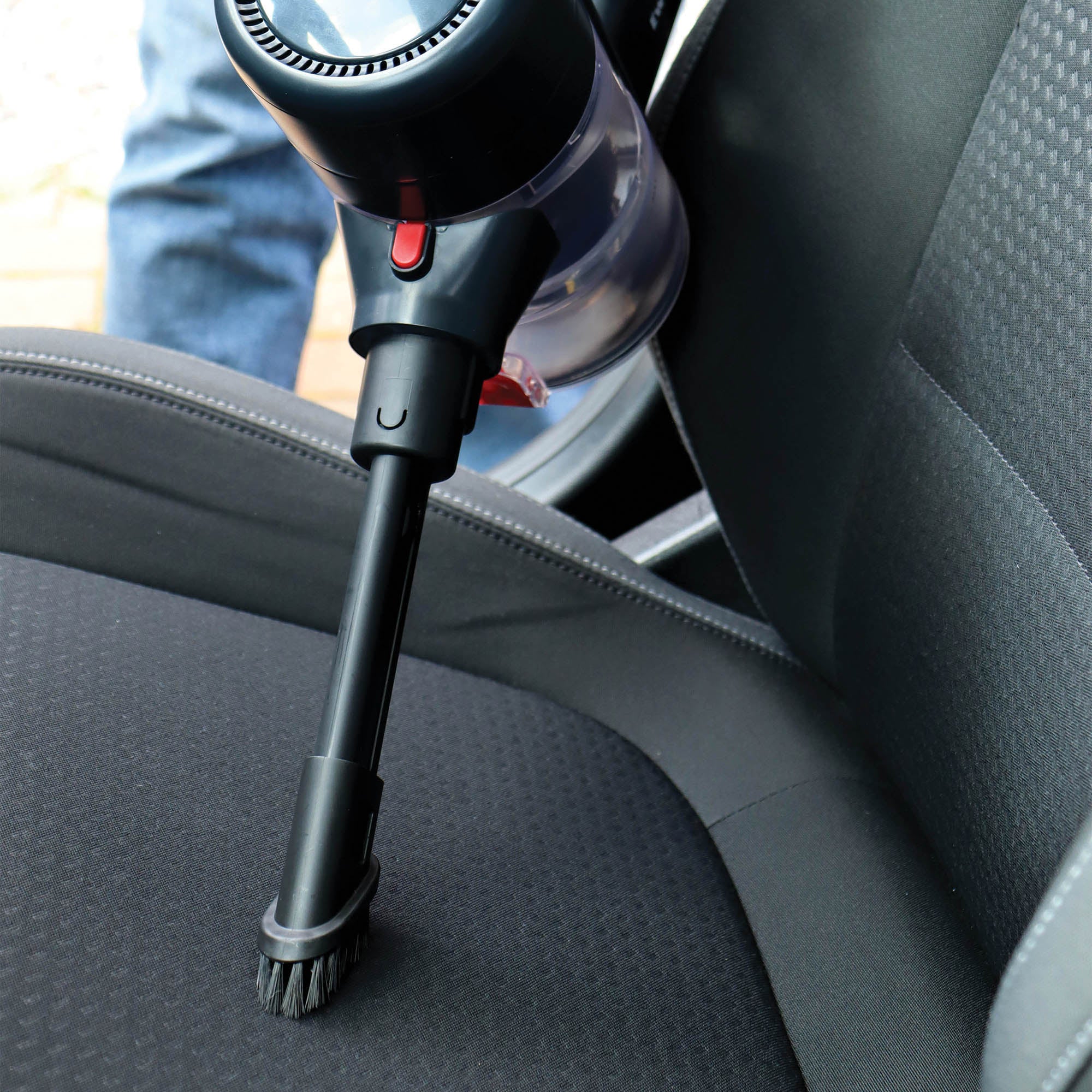 The AIRBLITZ 2-in-1 Cordless Stick Vacuum Cleaner, equipped with a brush attachment and washable HEPA filter, is being used to clean a car’s fabric seat for efficient dust and allergen removal.