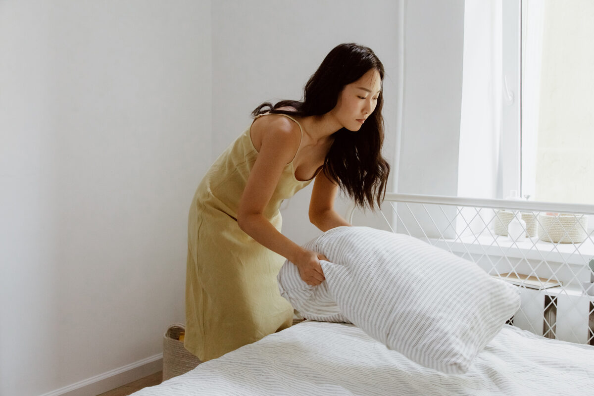 A woman changes bedding on a white bed